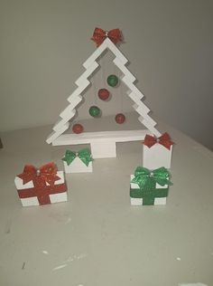 small christmas tree made out of white cardboard with green and red bows on it, sitting on a table