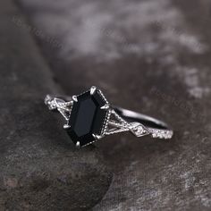 a black diamond ring sitting on top of a stone slab with diamonds around the band