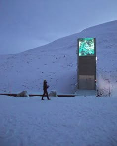 a person walking in the snow next to a tall tower with a tree on it