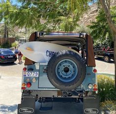 a jeep with a surfboard strapped to it's back end is parked in front of a palm tree