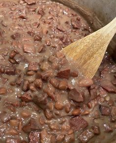 a pot filled with beans and meat next to a wooden spoon