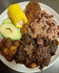 a white plate topped with meat, beans and corn on the cob next to an avocado