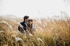 a man and woman are sitting in tall grass looking into each other's eyes