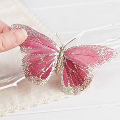 a pink butterfly sitting on top of a piece of cloth next to a person's hand