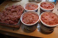 six plastic cups filled with food sitting on top of a wooden table next to tins