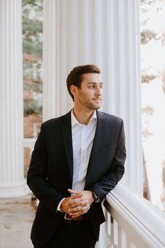 a man in a suit leaning against a white column with his hands on his hips