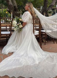 a woman wearing a wedding dress and veil standing in front of a table with chairs