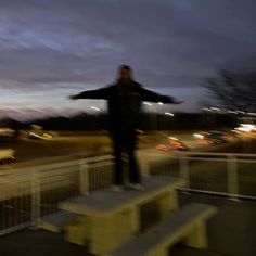 a man standing on top of a bench in front of a parking lot at night