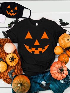 a black shirt with pumpkin faces on it next to other halloween decorations and face masks