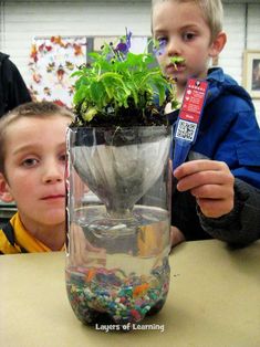 two boys sitting at a table with a plant in a glass vase on top of it