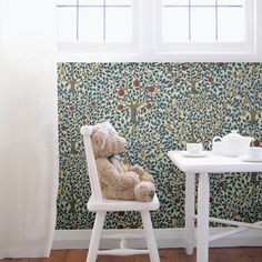 a teddy bear sitting on a chair in front of a wallpapered dining room