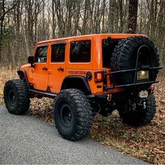 an orange jeep parked on the side of a road in front of trees and leaves