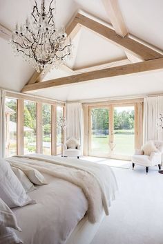 a bedroom with white furniture and chandelier hanging from the ceiling, along with large windows that look out onto a lush green field