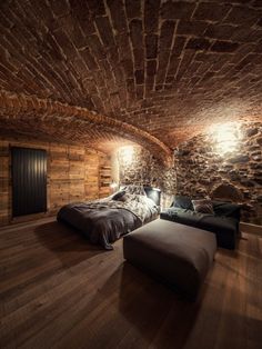 two beds in a room with brick walls and wood flooring, one is made up to