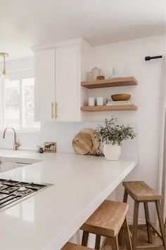 a kitchen with white counter tops and wooden stools next to a window covered in curtains