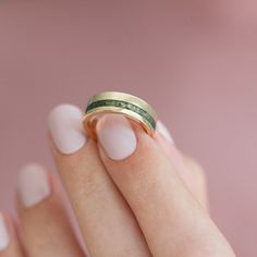 a woman's hand holding a gold and green wedding ring with two bands on it