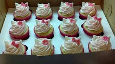 cupcakes with pink frosting and bows are in a box on the table