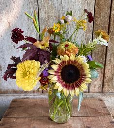 a vase filled with lots of flowers on top of a wooden table next to a wall