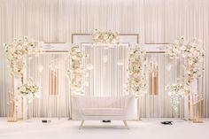 a white couch sitting in front of a wall covered in flowers and greenery with gold accents