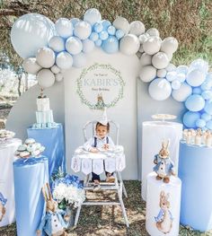 a baby is sitting in a highchair surrounded by blue and white balloons, bunnies, and cake