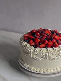 a white cake topped with berries and blueberries on top of a marble countertop