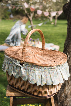 a wicker picnic basket sitting on top of a wooden stool next to a tree