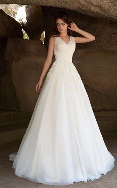 a woman in a white wedding dress standing next to a rock formation with her hand on her head