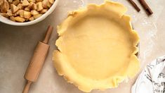 an uncooked pie crust sits next to a bowl of apples and cinnamon sticks