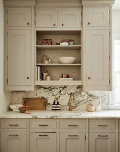 a kitchen with white cabinets and marble counter tops, along with an open shelf above the sink