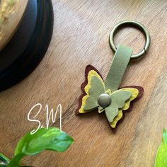 a butterfly shaped keychain sitting on top of a wooden table next to a plant