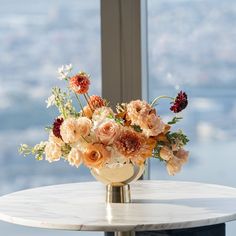 an arrangement of flowers on a table in front of a large window overlooking the city