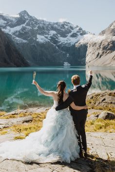 a bride and groom standing on the edge of a cliff with their arms in the air