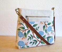 a white purse with blue and green flowers on it sitting on top of a wooden table