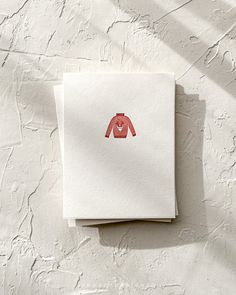 two pieces of paper with an image of a red sweater on it, sitting next to each other