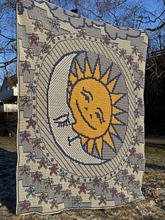 a quilt hanging on the side of a tree in front of a house with a smiling sun