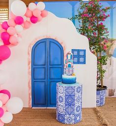 a blue and white table topped with a cake next to a wall covered in balloons