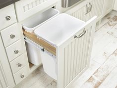 a kitchen with white cabinets and drawers has a trash can in the middle of it