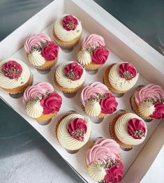 twelve cupcakes with pink and white frosting in a box on a table