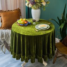 a green table cloth with plates and fruit on it in front of a vase filled with flowers