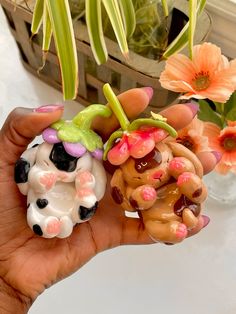 a hand holding two small figurines with flowers in the background