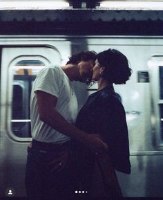 two people standing next to each other in front of a train