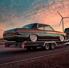 an old car is being towed by a flatbed truck with windmills in the background