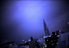 a very tall building with a sky line in the background and some buildings lit up at night