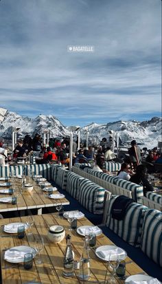 people are sitting at tables with plates and glasses on them in front of snow covered mountains