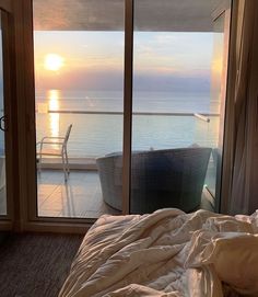 a bed sitting next to an open window on top of a wooden floor near the ocean