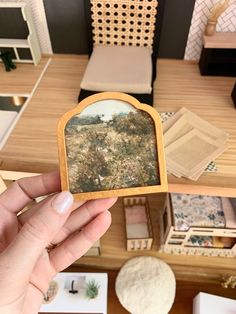 a person holding up a miniature photo in front of a table with chairs and pictures on it