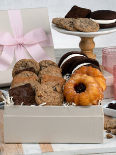 an assortment of cookies and pastries in a white box on a table with pink ribbon