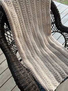 a crocheted blanket sitting on top of a wooden table next to a wicker chair