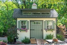 a small shed with flowers and potted plants on the outside, along with patio furniture