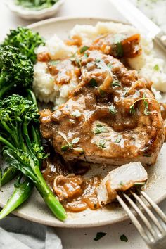 a white plate topped with meat and gravy next to broccoli